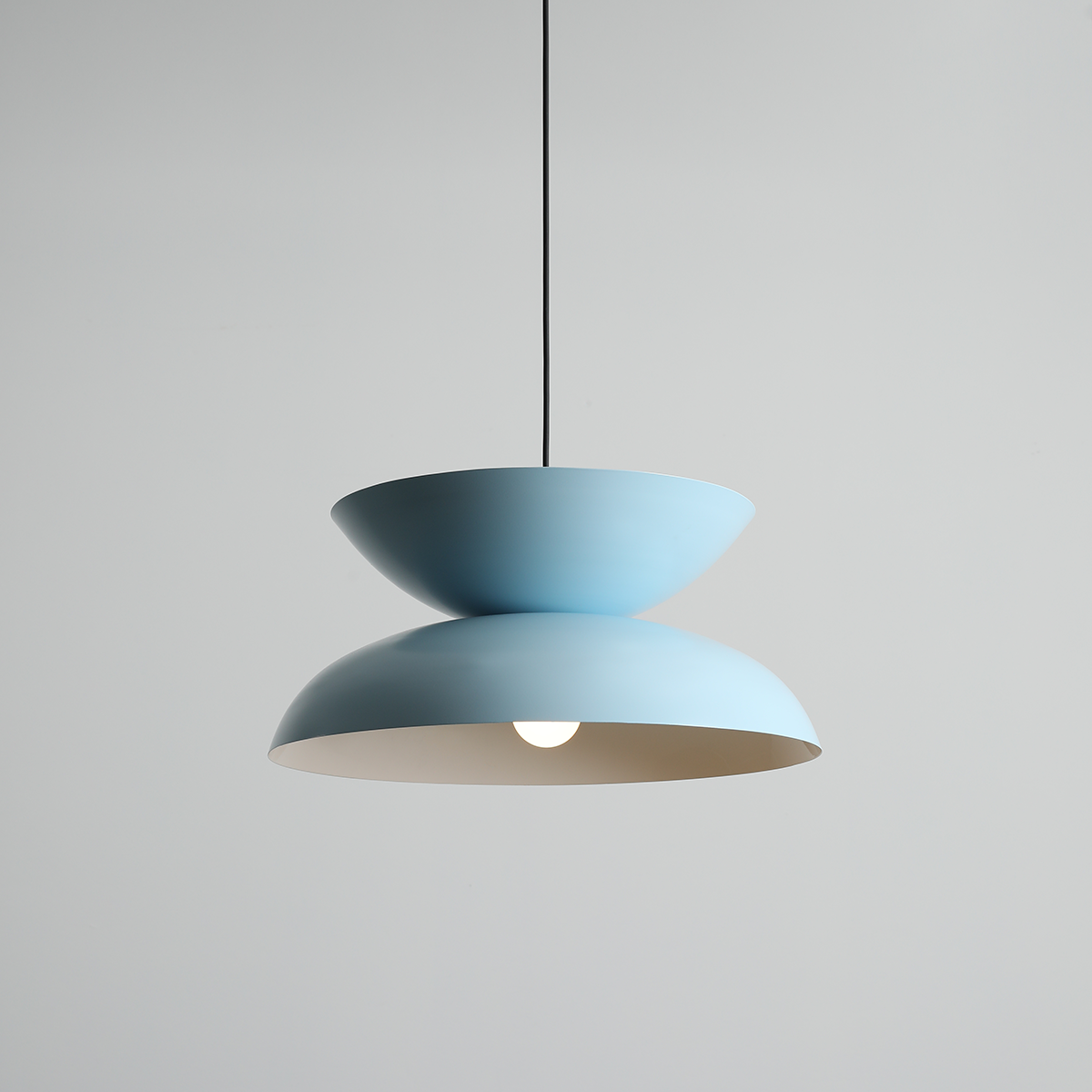 Lampa wisząca Millo w kolorze błękitnym, składająca się z dwóch połączonych części w kształcie misek. Utrzymana na czarnym przewodzie, z widoczną żarówką E27 w dolnej części. Tło jasnoszare, minimalistyczne.