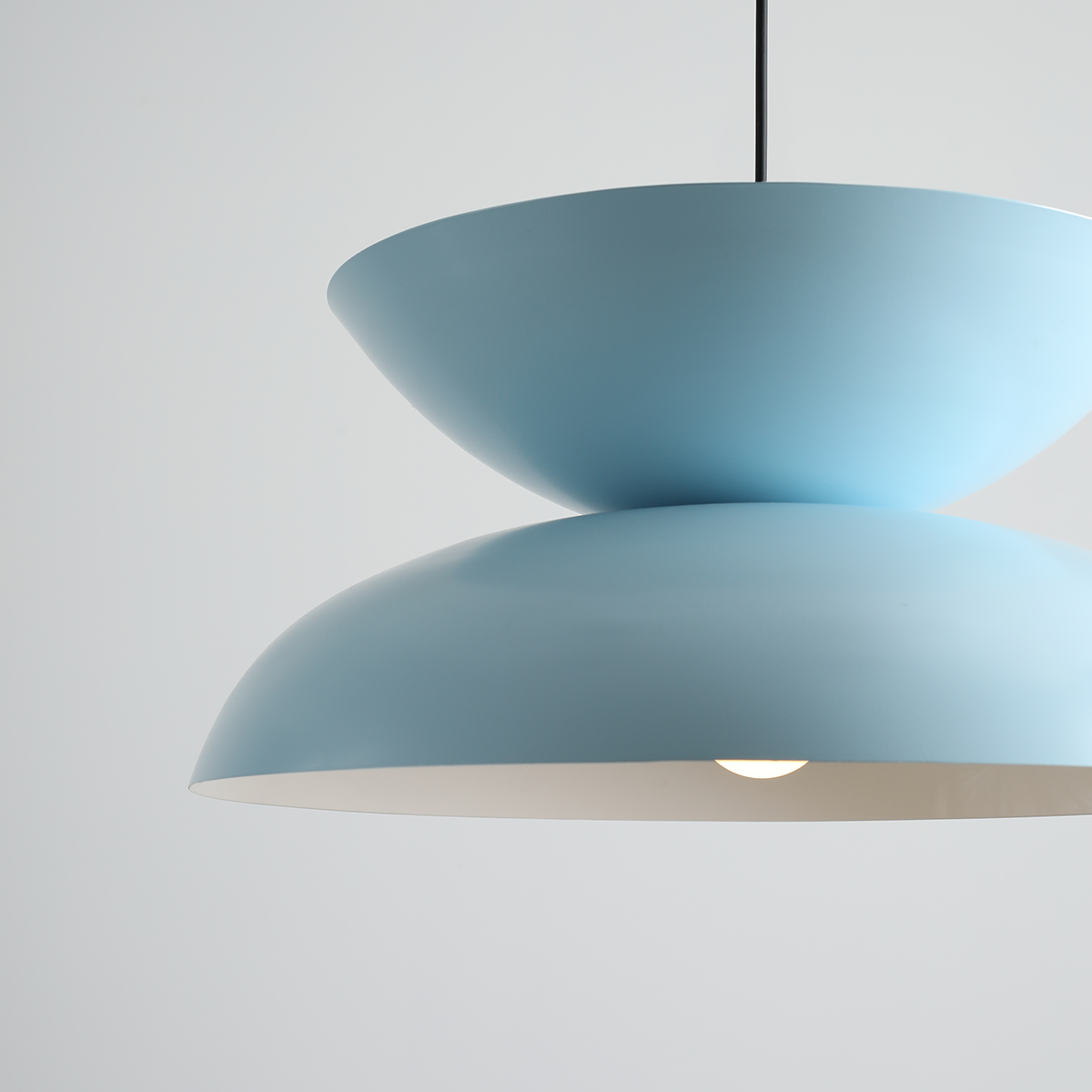 Lampa wisząca Millo w kolorze ciemnego błękitu, z dwoma połączonymi kloszami w kształcie misek. Ujęcie z przodu, z widocznością żarówki E27 w dolnej części klosza. Prosta, nowoczesna forma na czarnym kablu. Tło jasne, jednolite.
