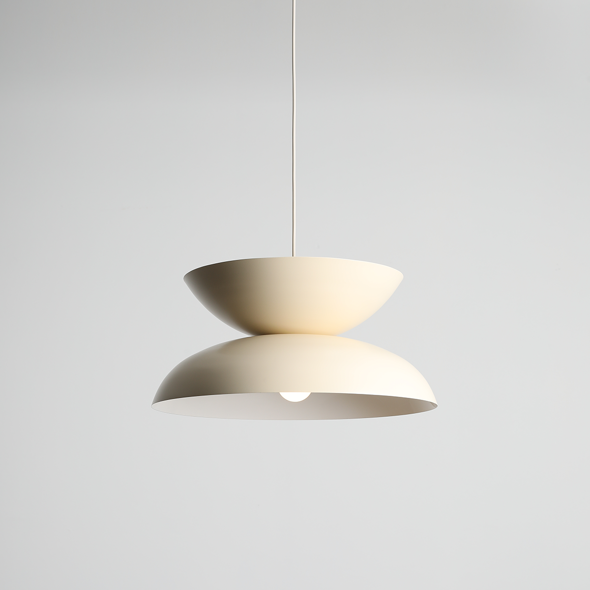 Lampa wisząca Millo w kolorze jasnego kremu, o nowoczesnym designie z dwoma półkulami, zawieszona na cienkim przewodzie. Dolna część lampy jest lekko wypukła, a środek jest otwarty, co eksponuje źródło światła.