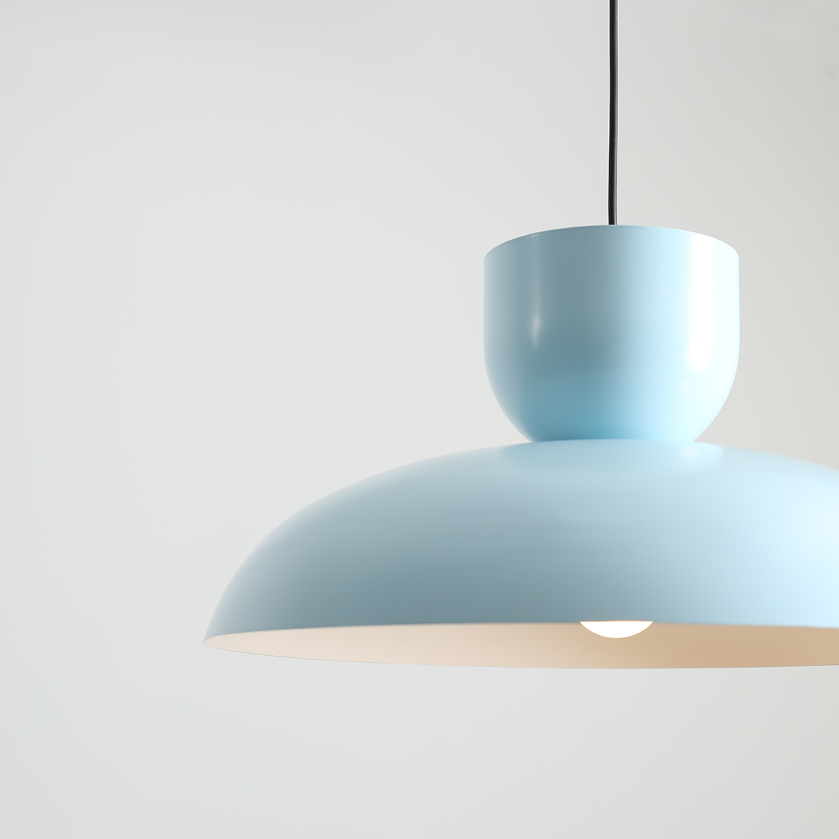 Lampa wisząca Ella w kolorze ciemnego błękitu, z cylindrycznym kloszem i gładką, matową powierzchnią. Zawieszona na czarnym przewodzie, idealna do nowoczesnych wnętrz. Klosz ma kształt półkuli, emitując ciepłe światło.