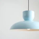 Lampa wisząca Ella w kolorze ciemnego błękitu, z cylindrycznym kloszem i gładką, matową powierzchnią. Zawieszona na czarnym przewodzie, idealna do nowoczesnych wnętrz. Klosz ma kształt półkuli, emitując ciepłe światło.