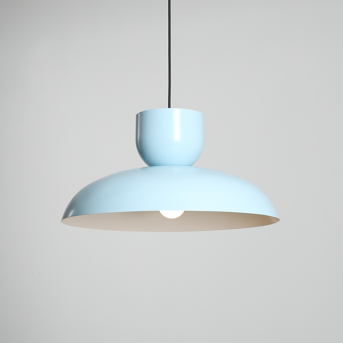 Lampa wisząca Ella w kolorze błękitnym, z metalowym kloszem o półkulistym kształcie. Produkt zawiera miejsce na żarówkę E27, zawieszony na czarnym przewodzie. Tło jednolite, jasne.