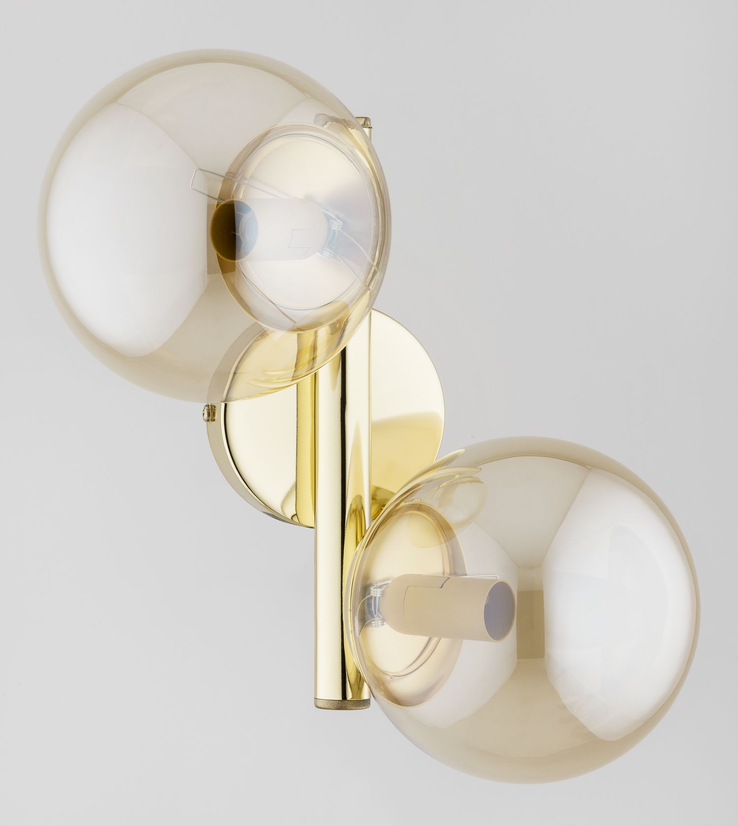 Kinkiet Eral 2xE14 w kolorze błyszczącego złota, z dwoma okrągłymi kloszami w przezroczystym odcieniu. Ujęcie frontalne, produkt zamontowany na ścianie, z widocznymi elementami mocującymi oraz otworami na żarówki.