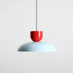Lampa wisząca Ella z jedną oprawą E27, z górną częścią w intensywnej czerwieni oraz dużym kloszem w odcieniu błękitnym. Produkt zawieszony na czarnym przewodzie, w prostym, neutralnym tle.