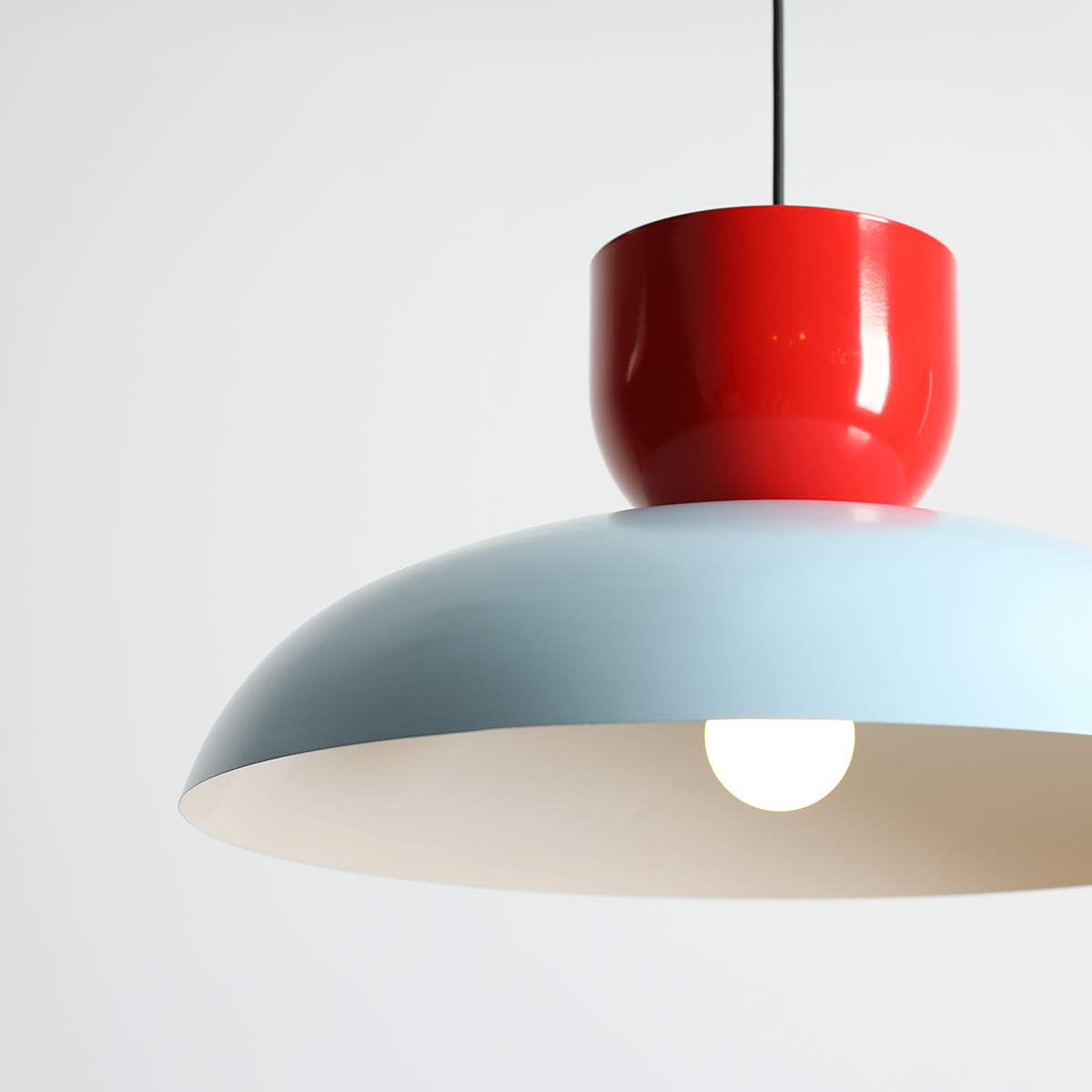 Lampa wisząca Ella z jedną oprawą E27 w kolorze ciemnego błękitu i czerwonej papryki. Posiada zaokrąglony klosz oraz okrągłą, błyszczącą podstawę. Zawieszona na czarnym kablu, idealna do nowoczesnych wnętrz.