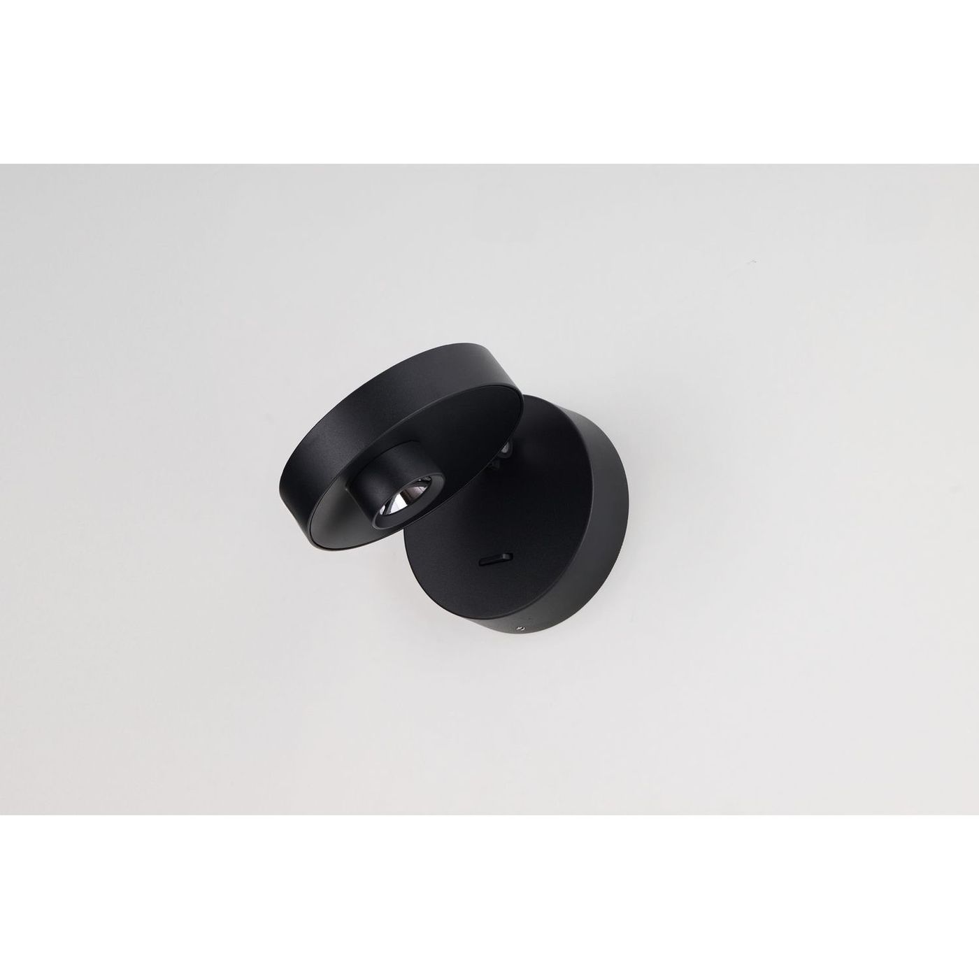 Iseo kinkiet spot LED 3W w kolorze czarnym, z okrągłą podstawą i cylindrycznym kloszem, zamontowany na ścianie. Kinkiet ma nowoczesny, minimalistyczny design, z widocznym źródłem światła skierowanym w dół. Tło proste, białe.