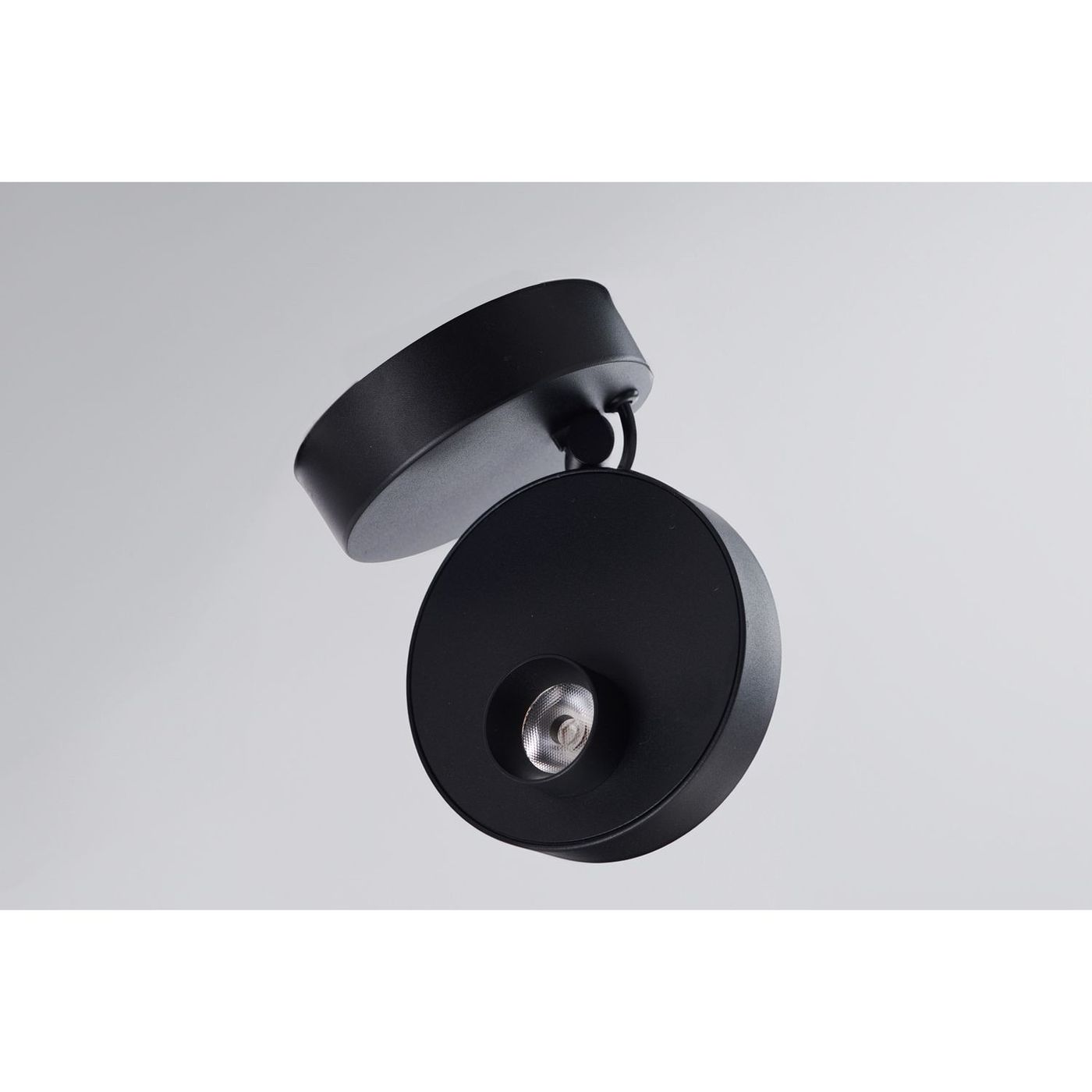 Lampa sufitowa spot LED 9W w kolorze czarnym, o okrągłej podstawie i obrotowym kloszu. Zainstalowana pod kątem, z widoczną diodą LED w centralnej części, na gładkim, jasnym tle.