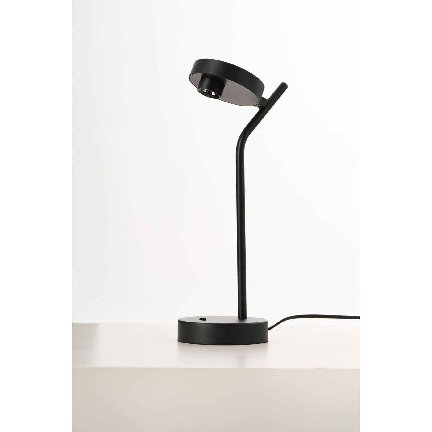 Czarna lampa stołowa LED Iseo o mocy 3W, z okrągłą podstawą i cienką, prostą nogą. Głowica lampy jest regulowana, co umożliwia skierowanie światła w wybrane miejsce. Produkt stoi na jasnym blacie, w minimalistycznym otoczeniu.