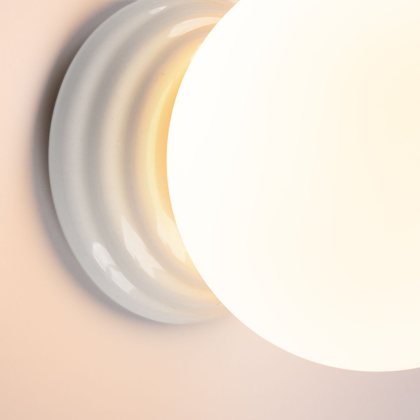 Biały kinkiet Zori z oprawą w kształcie falistej tarczy, z zamontowanym źródłem światła G9. Zbliżenie na detale, ukazujące gładką powierzchnię oraz subtelne oświetlenie. Produkt przeznaczony do użytku wewnętrznego, z klasą ochrony IP44.