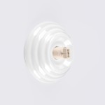 Biały kinkiet Zori z oprawą na żarówkę G9, z powierzchnią o lekkiej teksturze, w kształcie okrągłej, falistej tarczy. Produkt montowany na ścianie, z podświetlonym gniazdem, przeznaczony do użytku zewnętrznego (IP44).