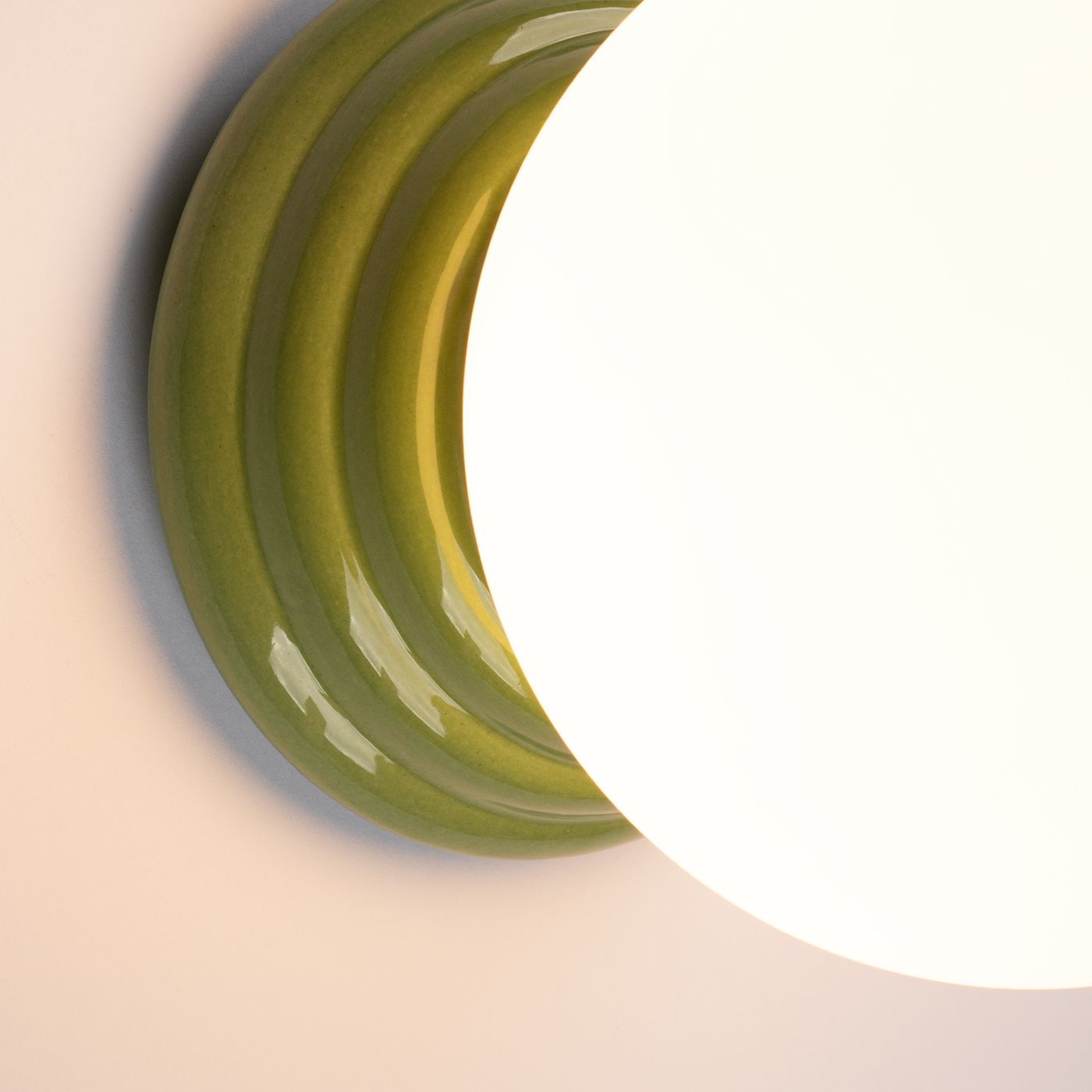 Zielony kinkiet Zori z ceramiczną podstawą w falistym kształcie, na której znajduje się okrągła, biała oprawa. Widoczny połysk materiału. Produkt przeznaczony do montażu ściennego, klasyfikacja IP44, co zapewnia odporność na wilgoć.