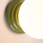 Zielony kinkiet Zori z ceramiczną podstawą w falistym kształcie, na której znajduje się okrągła, biała oprawa. Widoczny połysk materiału. Produkt przeznaczony do montażu ściennego, klasyfikacja IP44, co zapewnia odporność na wilgoć.