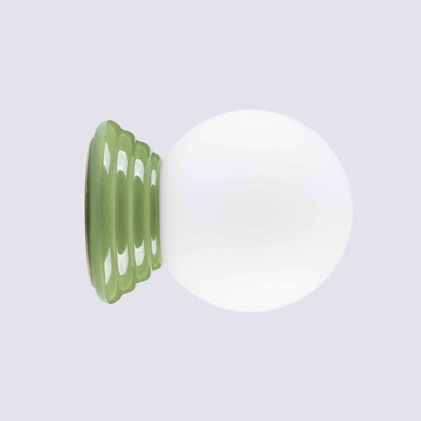 Zielony kinkiet Zori z podstawą w falistym kształcie i białą, okrągłą szklaną kopułą. Produkt ustawiony na płaskiej powierzchni, z widoczną strukturą podstawy. Idealny do wnętrz, spełnia wymogi IP44.