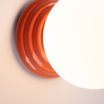 Kinkiet Zori 1xG9 IP44 w kolorze brzoskwiniowym, z ceramiczną podstawą o falistym kształcie i matową, okrągłą oprawą na żarówkę. Produkt ukazany z góry, z widoczną gładką powierzchnią podstawy.