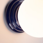 Kinkiet Zori w kolorze ultramaryny z okrągłą, białą kloszem. Ujęcie z góry, pokazujące gładką, błyszczącą podstawę z wyraźnymi, zaokrąglonymi krawędziami. Produkt przeznaczony do montażu na ścianie, z zabezpieczeniem IP44.