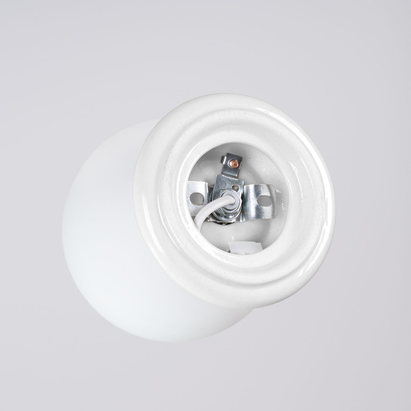 Biała lampa sufitowa Zori z oprawą na jedną żarówkę G9, widok z góry. Ceramiczna podstawa z metalowymi mocowaniami i przewodami wewnętrznymi. Prosta, okrągła forma, idealna do nowoczesnych wnętrz.