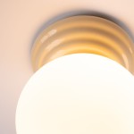Beżowa lampa sufitowa Zori z oprawą w kształcie okrągłej, gładkiej, matowej klosza oraz dekoracyjnym pierścieniem. Ujęcie z dołu, ukazujące detale wykończenia oraz źródło światła G9. Idealna do pomieszczeń z ograniczoną przestrzenią.