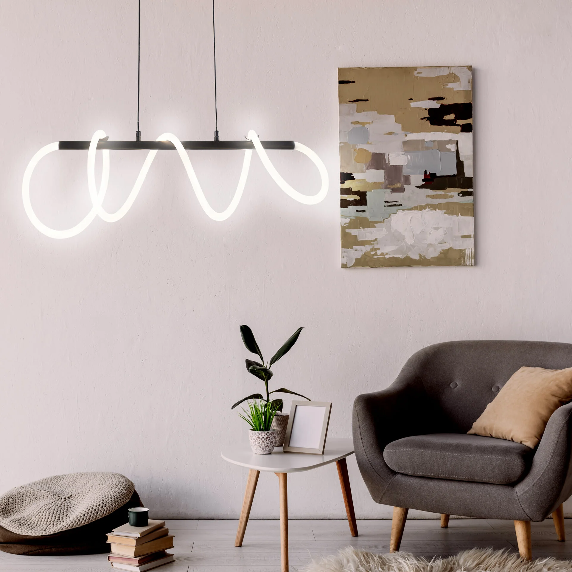 Lampa wisząca LED Emma 85W 4000K w kolorze czarnym, o nowoczesnym, falistym kształcie. Zawieszona na dwóch przewodach, emituje jasne światło. W tle widoczny stół z rośliną i obraz na ścianie, w aranżacji nowoczesnego wnętrza.