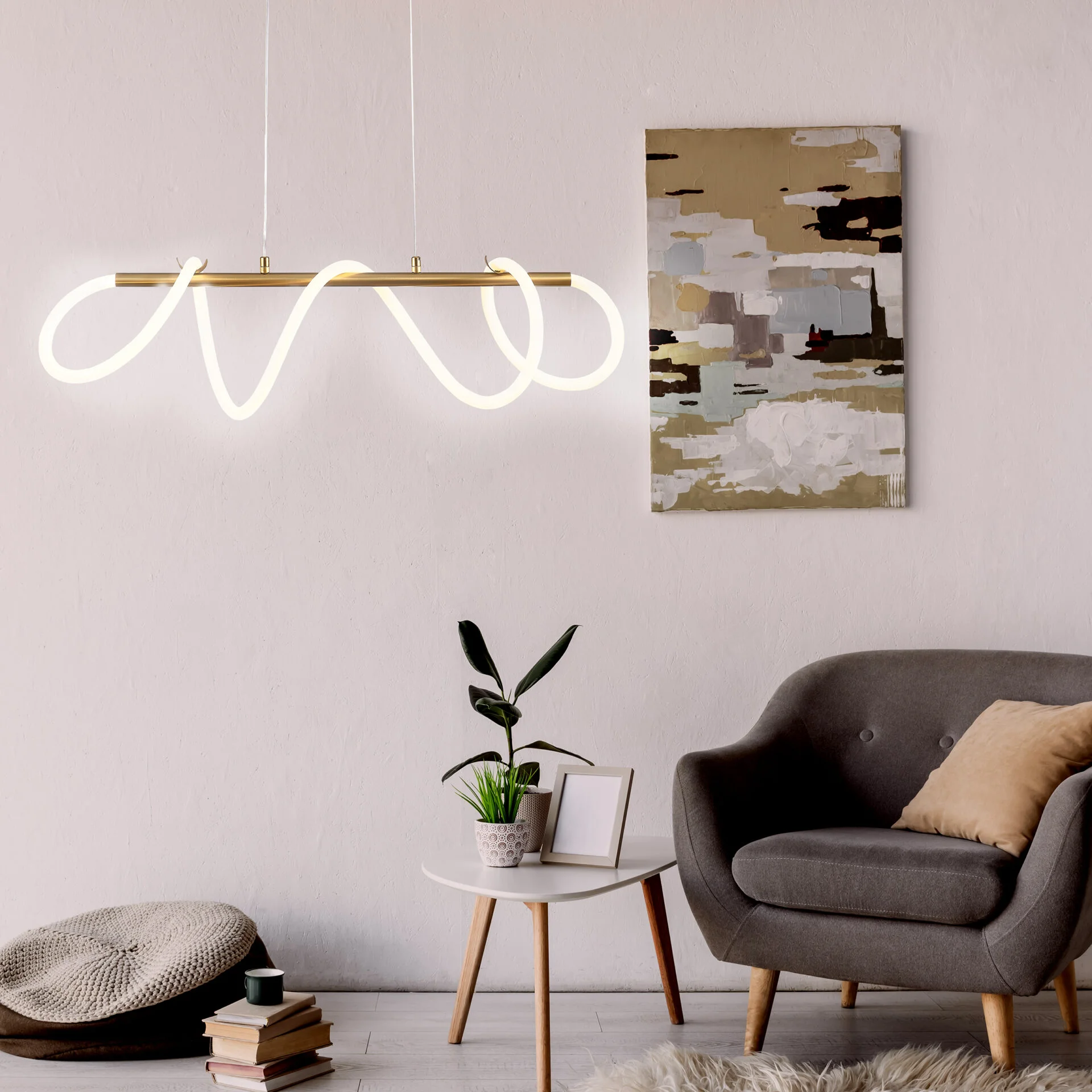 Lampa wisząca LED Emma o mocy 85W i temperaturze barwowej 4000K, złota, z unikalnym, falistym kształtem. Zawieszona nad stolikiem, w otoczeniu roślin i dekoracji, w nowoczesnym wnętrzu.