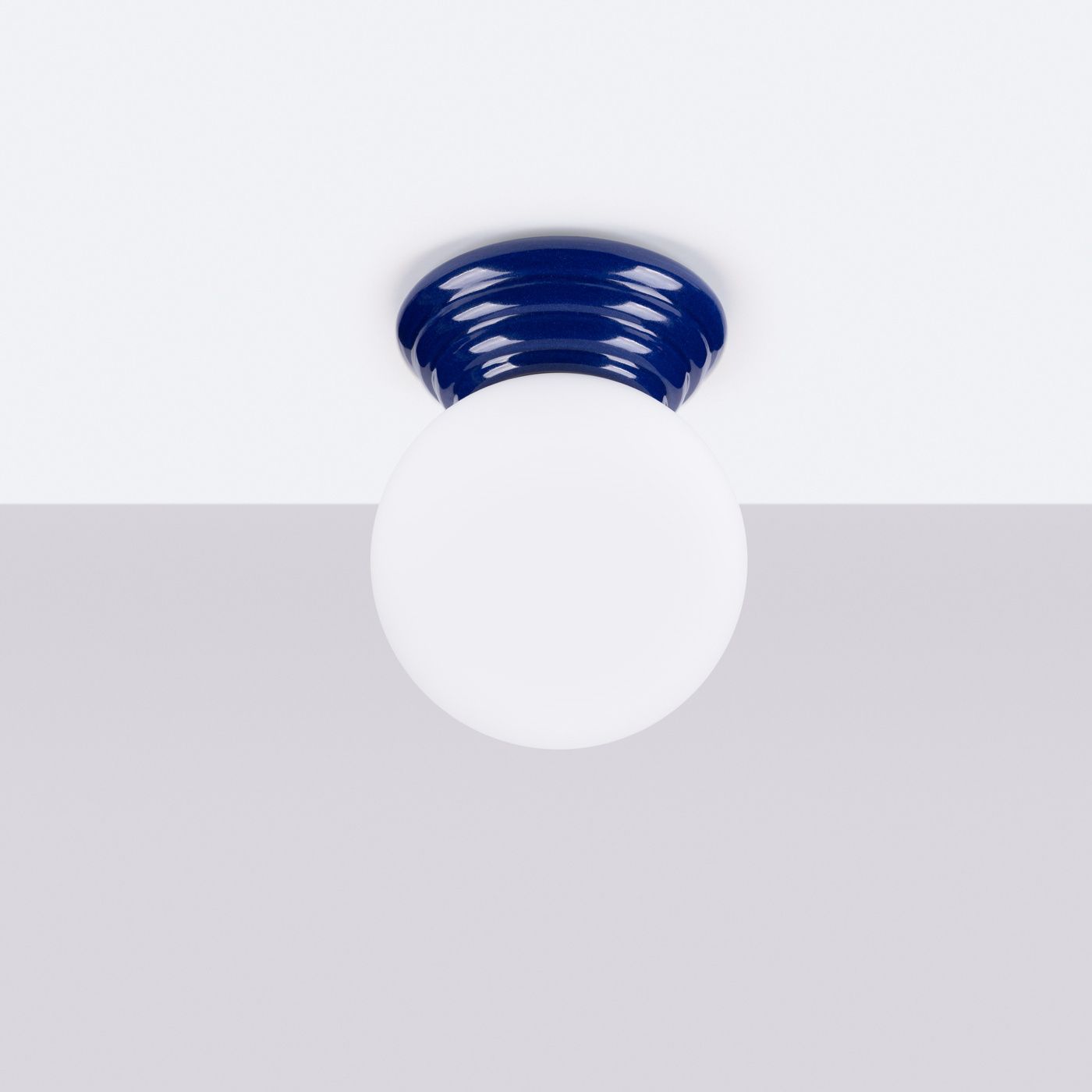 Lampa sufitowa Zori 1xG9 IP44 w kolorze ultramaryny z okrągłym, białym kloszem. Widok z dołu, zamontowana na białym suficie. Gładka, błyszcząca podstawa z dekoracyjnym, falistym wzorem.