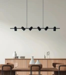 Lampa wisząca Vivi w kolorze czarnym, z sześcioma punktami świetlnymi GU10. Ujęcie frontalne, zawieszona nad drewnianym stołem, na tle jasnej ściany. W widoku widać również dekoracyjne wazony i książki na komodzie.