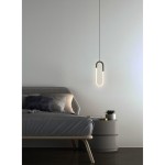 Lampa wisząca LED Nexus 9W w czarnej obudowie o kształcie elipsy, zawieszona nad łóżkiem w sypialni. Światło emitowane przez lampę ma ciepły odcień, a tło jest jasne, minimalistyczne, z meblami w neutralnych kolorach.