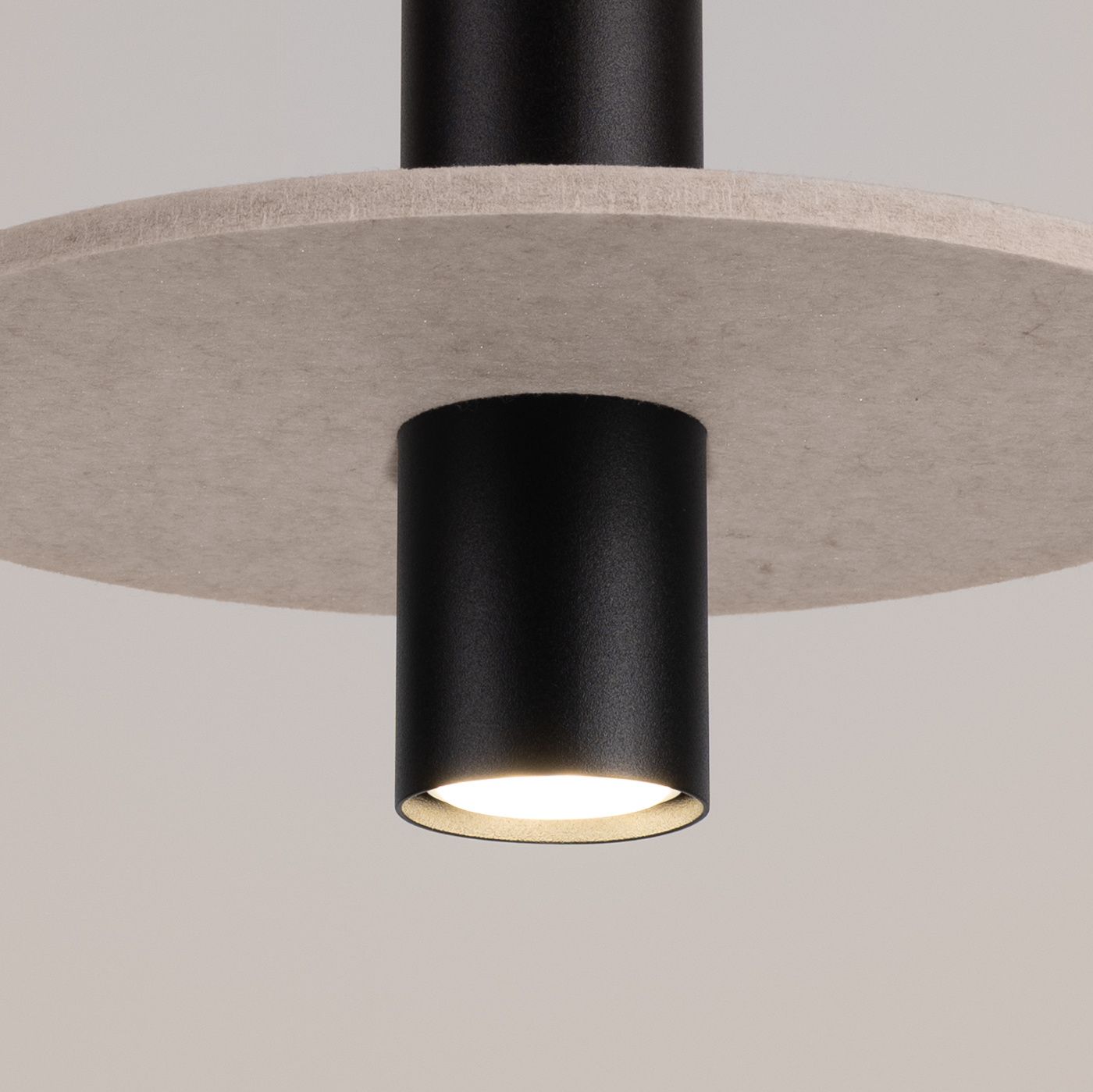 Lampa wisząca Pelta z jedną oprawą GU10, w kolorze czarnym i beżowym. Widoczny czarny korpus z metalowym wykończeniem oraz beżowy, okrągły klosz z materiału. Produkt zawieszony w pozycji pionowej, zbliżenie na detal oprawy.