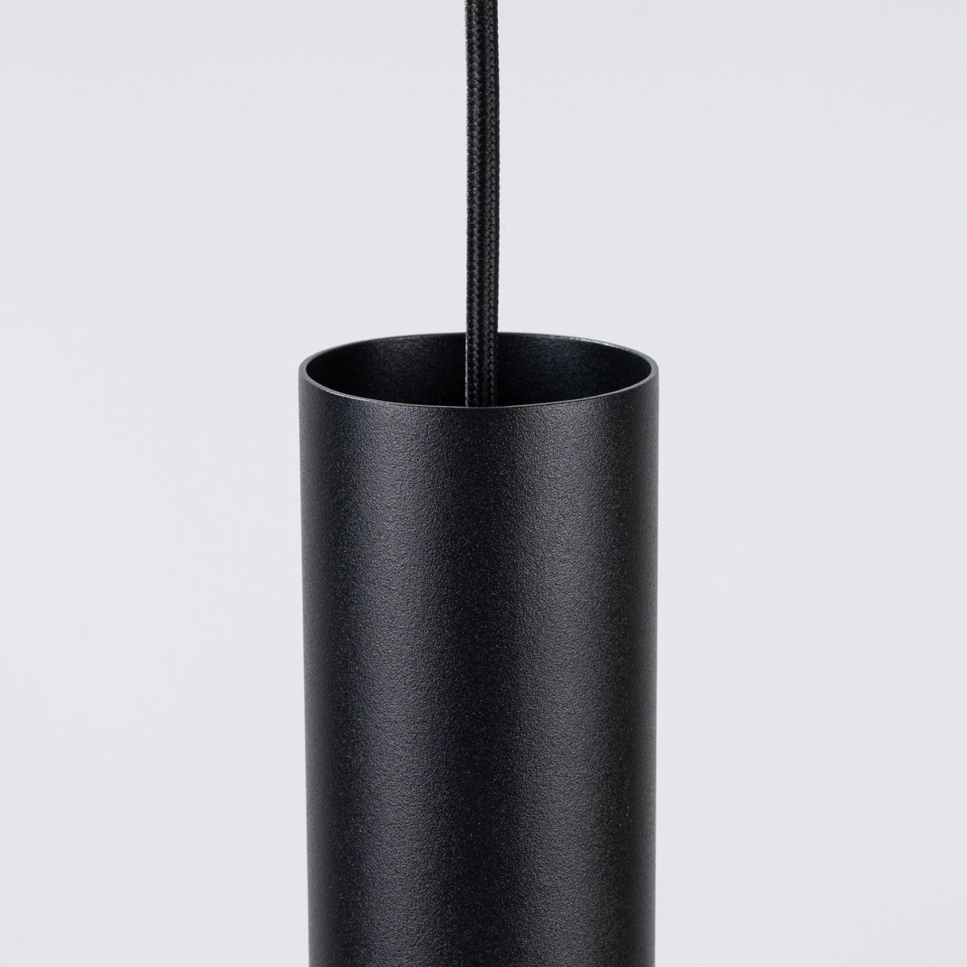 Lampa wisząca Pelta w kolorze czarnym z metalowym, cylindrycznym kloszem. Widoczny kabel w oplocie. Produkt w ujęciu z góry, ukazujący detal górnej części lampy. Idealna do nowoczesnych wnętrz.