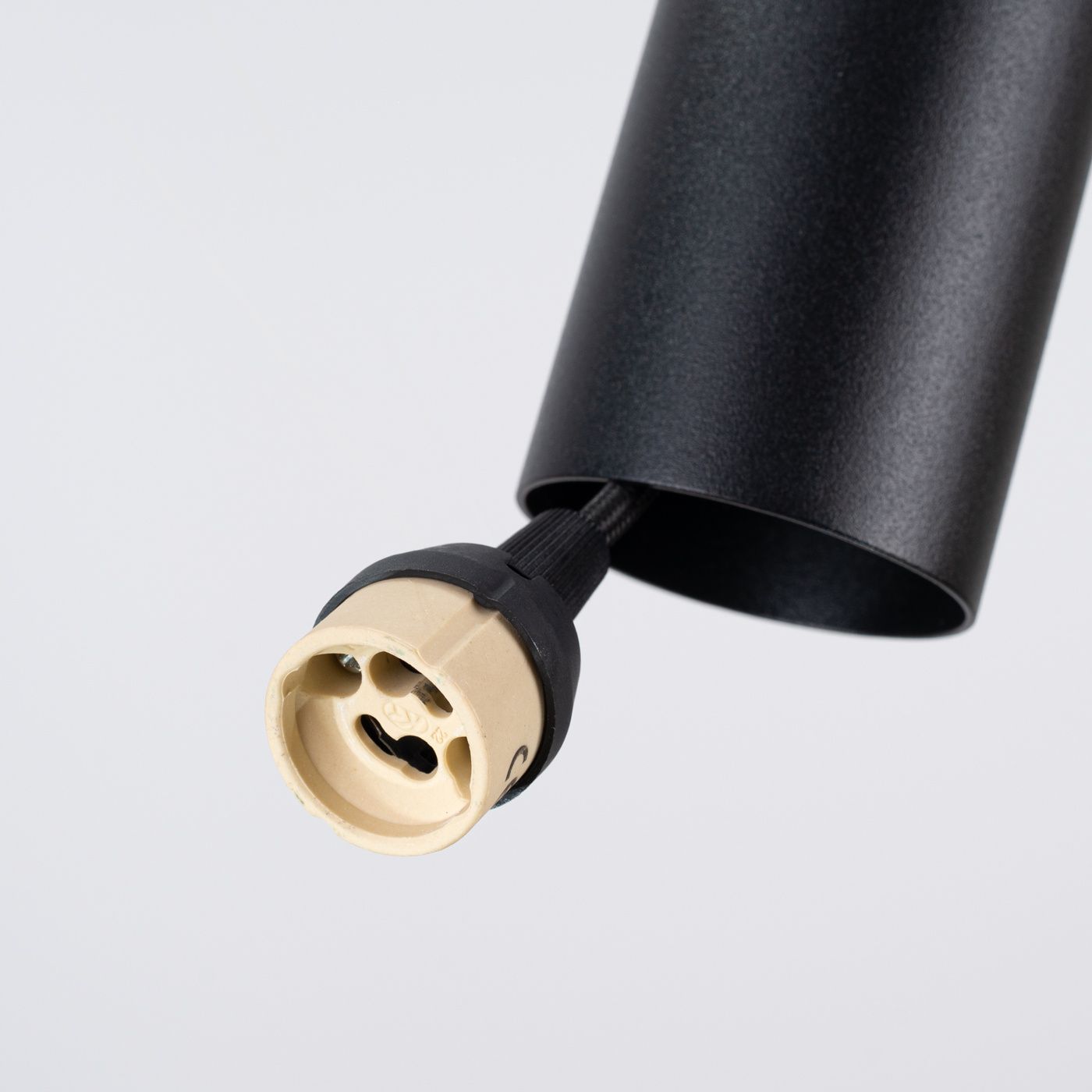 Lampa wisząca Pelta w kolorze czarnym z żółtym gniazdem GU10. Widoczny detal to mocowanie żarówki z czarnym uchwytem oraz cylindryczny korpus. Produkt uchwycony z bliska, na jasnym tle.