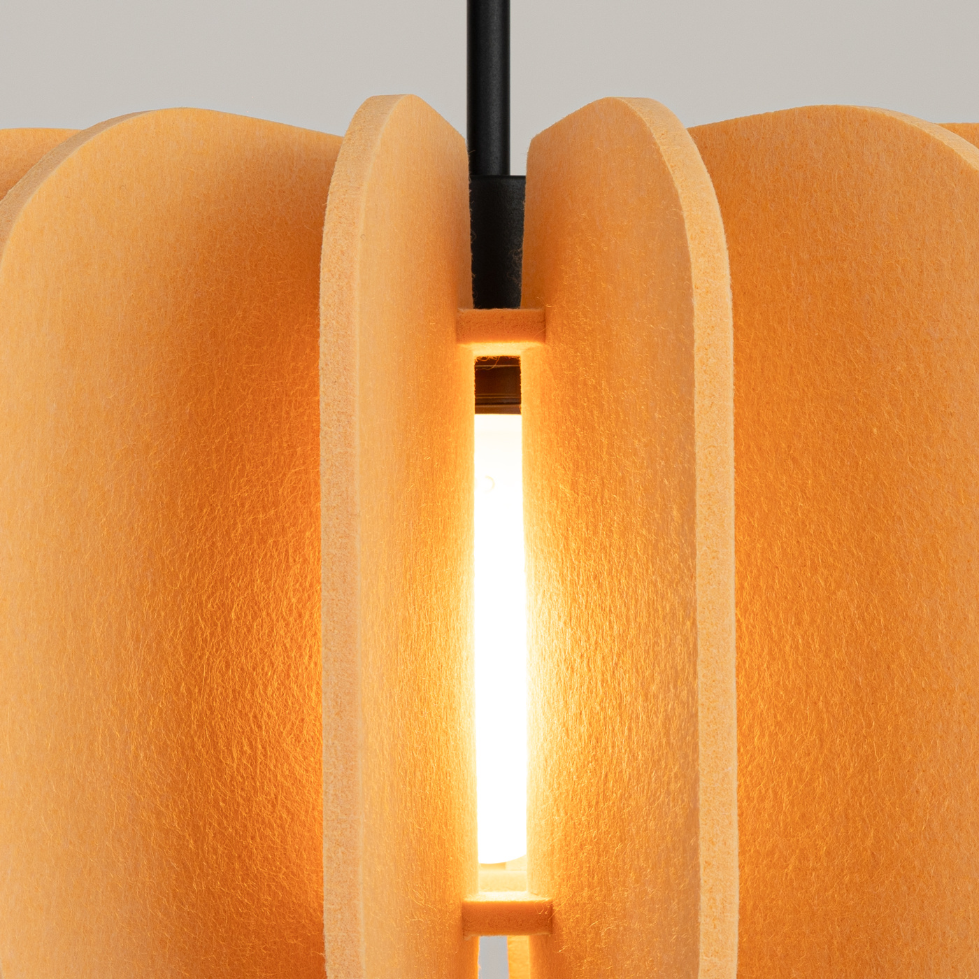 Lampa wisząca Mula D45 z materiału w kolorze czarnym i żółtym, z widocznym źródłem światła E27. Konstrukcja z falistymi, teksturowanymi panelami, zawieszona na cienkim, czarnym przewodzie. Ujęcie z bliska, koncentrujące się na detalu obudowy.