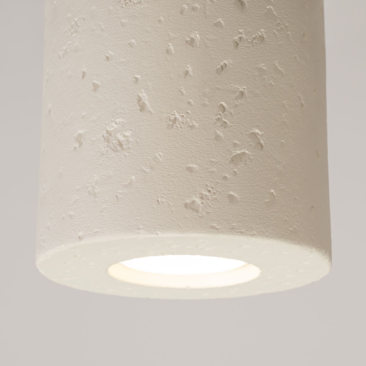 Beżowa lampa sufitowa Orbis Beton z oprawą na jedną żarówkę GU10. Okrągły klosz z teksturą, widoczna neutralna barwa i delikatne wypukłości. Ujęcie w zbliżeniu na górną część lampy z widocznym wnętrzem klosza.