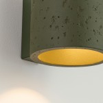 Kinkiet Orbis Beton 1xG9 w kolorze oliwkowym z matowym, betonowym wykończeniem i złotym wnętrzem klosza. Ujęcie z boku, montowany na ścianie, podkreślający teksturę materiału oraz kontrast kolorów.