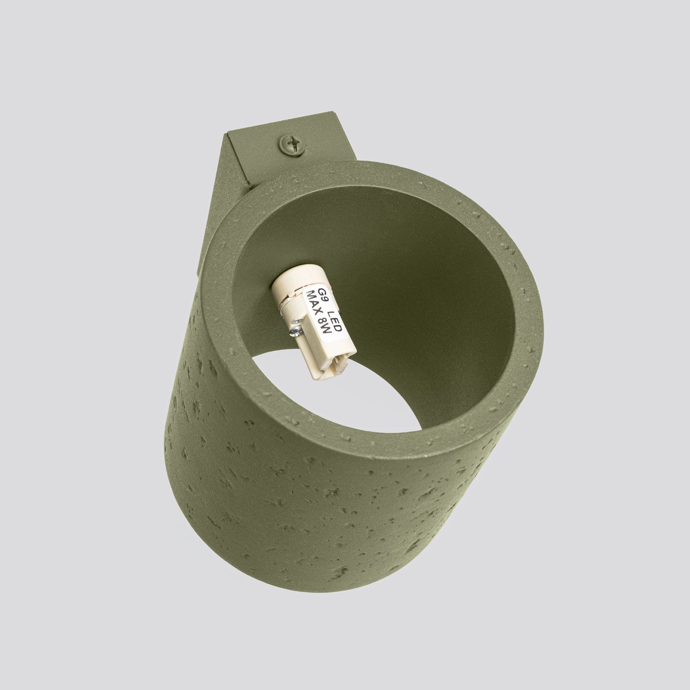 Kinkiet Orbis Beton 1xG9 w kolorze zielonej oliwki, wykonany z betonu, o cylindrycznym kształcie. Widoczne gniazdo na żarówkę G9. Ujęcie z góry, ukazujące teksturę materiału oraz detal montażowy. Tło proste, szare.