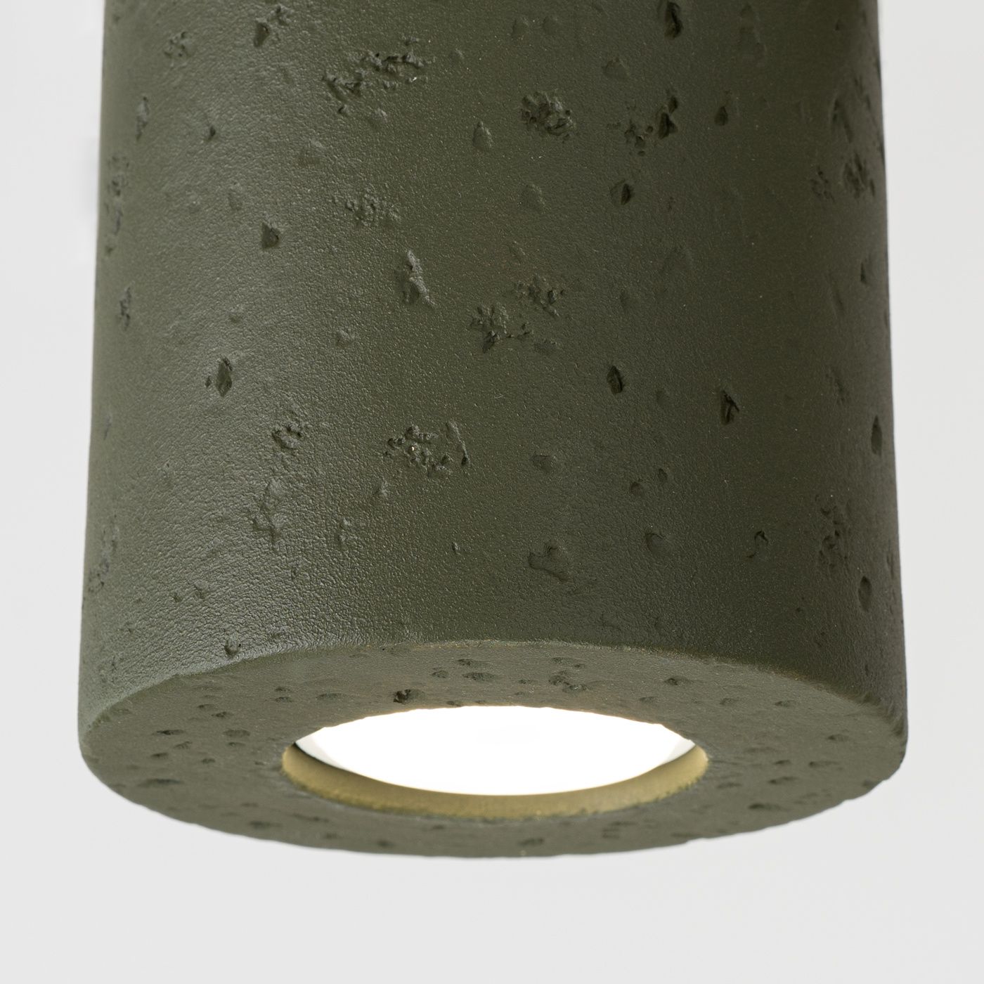 Lampa sufitowa Orbis Beton w kolorze oliwkowej zieleni, wykonana z teksturowanego betonu. Cylindryczny kształt z widocznym otworem na żarówkę GU10, zawieszona w pozycji pionowej. Tło proste, białe.