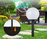 Lampa solarna ogrodowa Ballo D10/H34 w białej, okrągłej oprawie z przezroczystym kloszem, umieszczona na czarnym słupku. W tle widoczna aranżacja ogrodu z zielenią i meblami ogrodowymi. W zbliżeniu widoczny sposób montażu w ziemi.