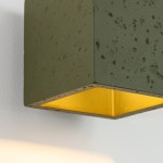 Kinkiet Quad Beton 1xG9 w kolorze oliwkowej zieleni, wykonany z betonu. Kwadratowy kształt z matową powierzchnią, z wewnętrzną złotą refleksją, zamontowany na ścianie. Widoczny detal struktury betonu.