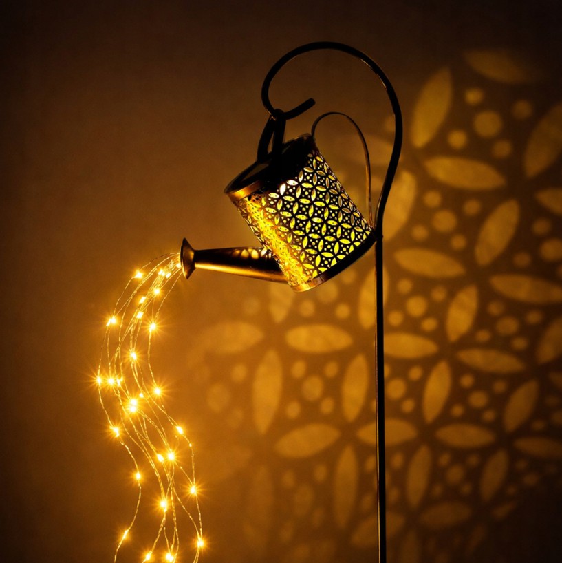 Konewka solarna lampa ogrodowa, w kształcie metalowej konewki z ażurowym wzorem, emituje ciepłe światło LED. Wbijana w ziemię, z efektem świetlnym tworzącym wzory na tle. Wysokość 80 cm.
