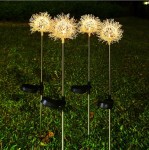 Dmuchawiec lampa solarna ogrodowa H76 LED, składająca się z czterech złotych, dekoracyjnych główek w kształcie dmuchawca na metalowych stelażach, wbitych w zieloną trawę. Lampa emituje ciepłe światło, idealna do oświetlenia ogrodu.