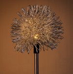 Lampa solarna Dmuchawiec o wysokości 76 cm, wbijana w ziemię. Kluczowy element to okrągła, metalowa konstrukcja w kształcie dmuchawca z delikatnymi, świecącymi diodami LED w środku. Stojąca, z prostym, czarnym stelażem.