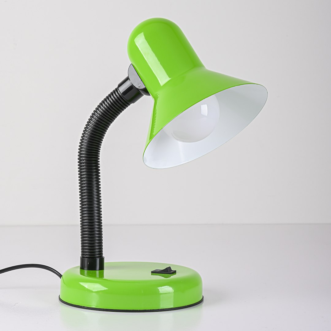 Zielona lampka biurkowa Mentor z kloszem w kształcie dzwonu i elastycznym ramieniem. Posiada okrągłą, zieloną podstawę z przyciskiem oraz czarną, teksturowaną rurkę. Klosz ma białe wnętrze, co umożliwia lepsze rozpraszanie światła.