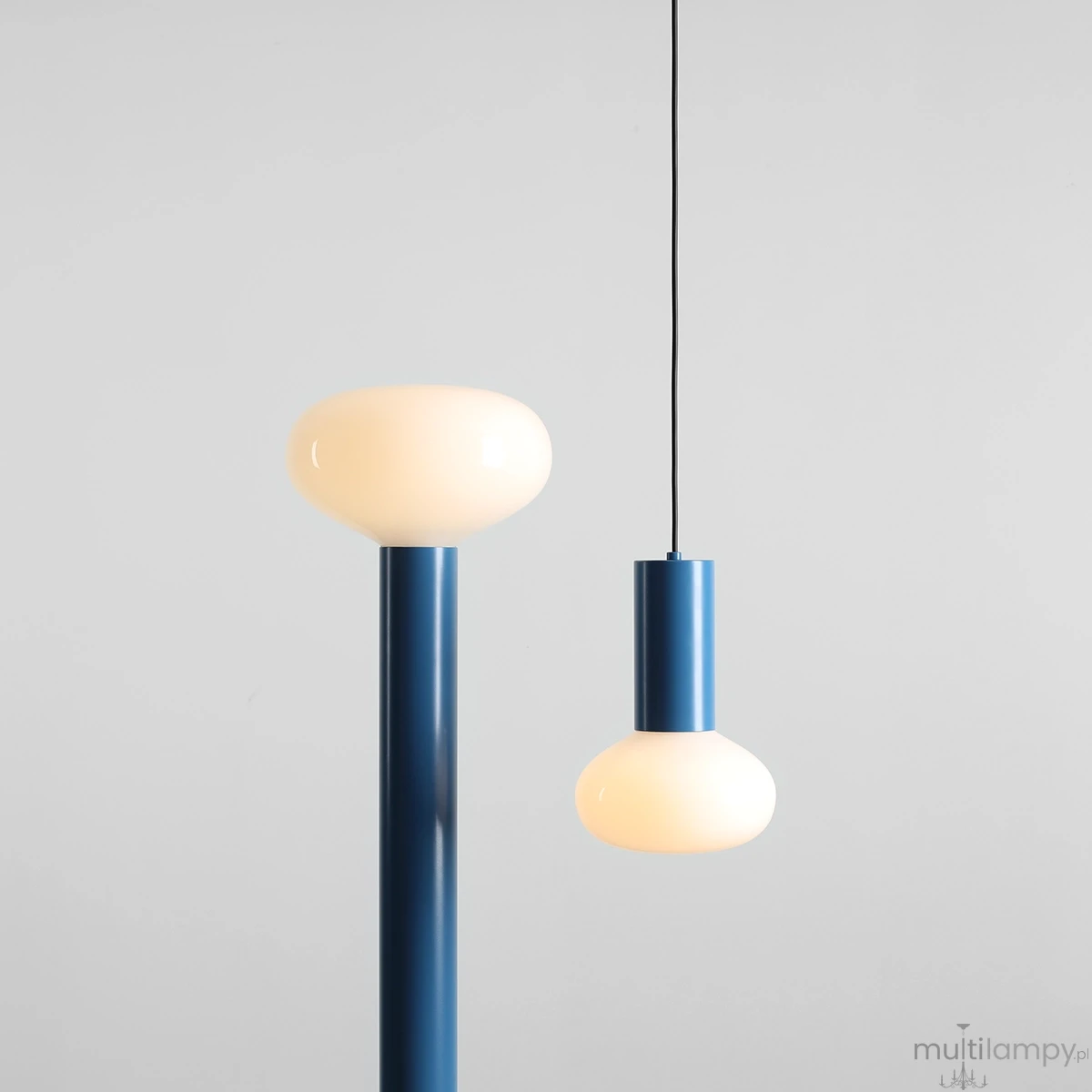 Lampa wisząca Flo Sky D19 z jedną oprawą E14, w kolorze niebieskim. Posiada okrągłą, matową klosz w kształcie kropli oraz prostą, smukłą konstrukcję. Zawieszona na cienkim, czarnym przewodzie. Tło jasne, minimalistyczne.