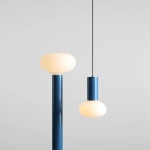 Lampa wisząca Flo Sky D19 z jedną oprawą E14, w kolorze niebieskim. Posiada okrągłą, matową klosz w kształcie kropli oraz prostą, smukłą konstrukcję. Zawieszona na cienkim, czarnym przewodzie. Tło jasne, minimalistyczne.