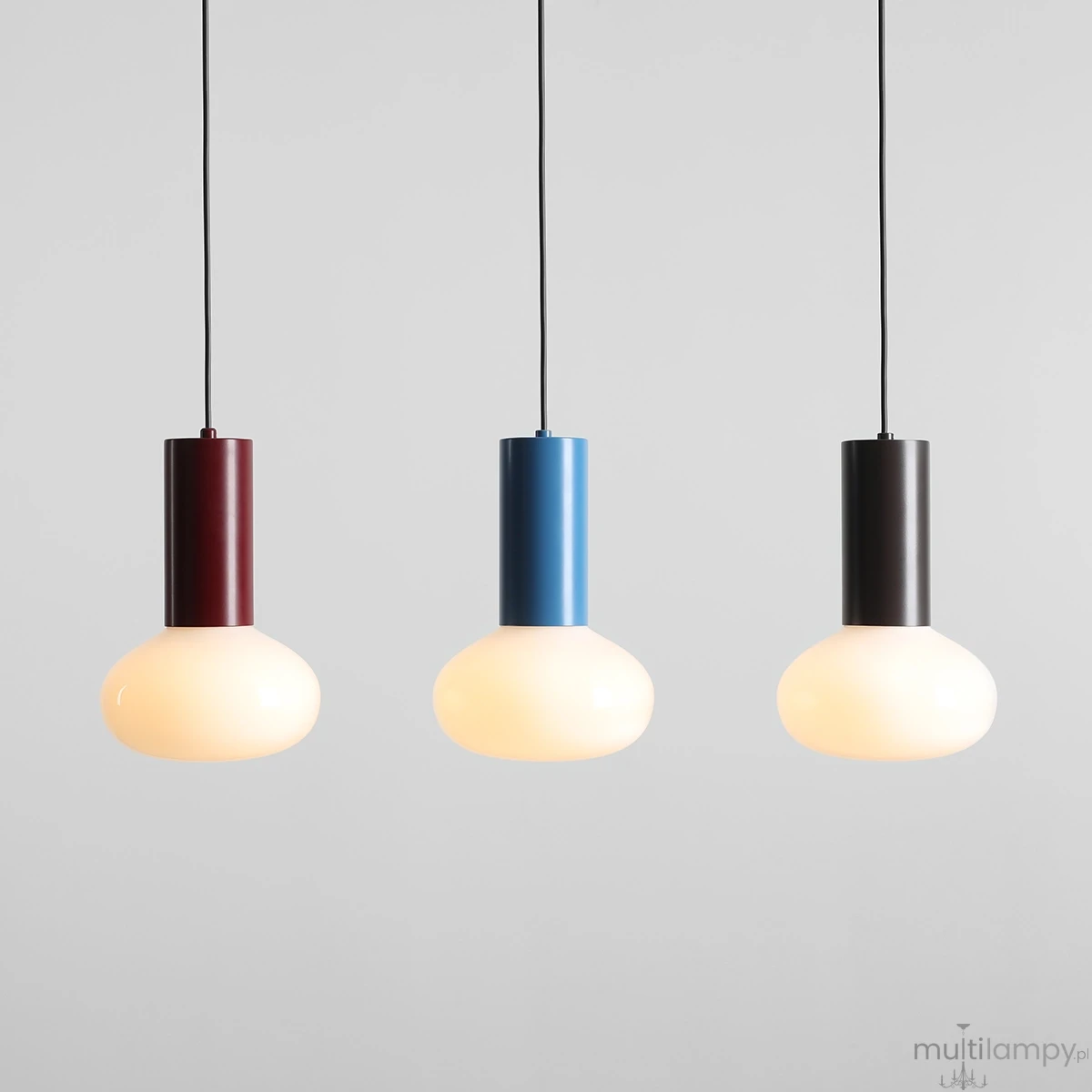 Lampa wisząca Flo Sky D19 z trzema kolorowymi abażurami: burgundowym, niebieskim i czarnym. Okrągłe, matowe klosze w kształcie kuli, zawieszone na czarnych przewodach, na jednolitym szarym tle.