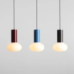 Lampa wisząca Flo Sky D19 z trzema kolorowymi abażurami: burgundowym, niebieskim i czarnym. Okrągłe, matowe klosze w kształcie kuli, zawieszone na czarnych przewodach, na jednolitym szarym tle.