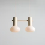 Lampa wisząca Flo Cream z dwoma kloszami E14, w kolorze kremowym. Klosze mają zaokrąglony kształt, a całość podwieszona jest na cienkich linkach. Elementy metalowe w neutralnym odcieniu, minimalistyczny design. Tło jasne, proste.