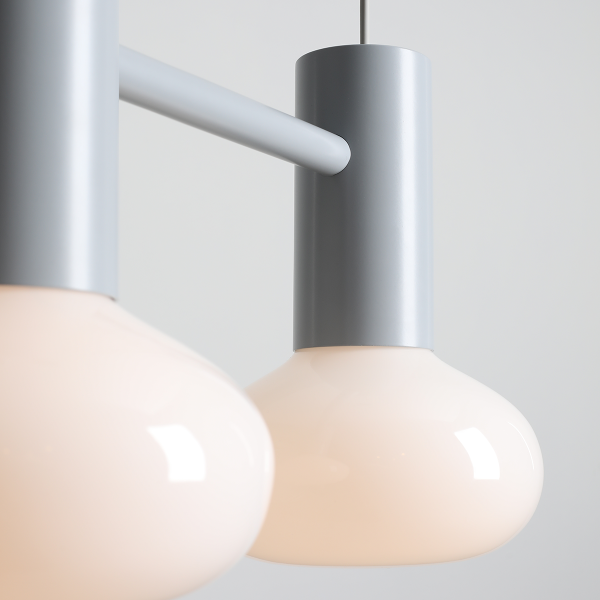 Lampa wisząca Flo Grey z dwoma kloszami w kształcie kropli, wykonana z matowego szkła w odcieniu jasnego różu. Elementy metalowe w kolorze szarym, zawieszenie na cienkim kablu. Kąt ujęcia zbliżenie na detale lampy.