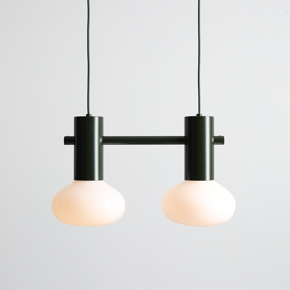 Lampa wisząca Flo Moss z dwoma kloszami w kolorze mleczno-białym, zawieszona na zielonym, matowym stelażu. Klosze mają okrągły kształt, całość utrzymana w nowoczesnym stylu, idealna do różnych aranżacji wnętrz.