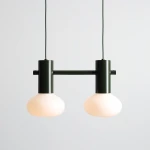 Lampa wisząca Flo Moss z dwoma kloszami w kolorze mleczno-białym, zawieszona na zielonym, matowym stelażu. Klosze mają okrągły kształt, całość utrzymana w nowoczesnym stylu, idealna do różnych aranżacji wnętrz.