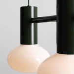 Lampa wisząca Flo Moss 2xE14 z zielonym, matowym metalowym mocowaniem i dwoma okrągłymi kloszami w delikatnym różowym odcieniu. Produkt zawieszony, z widocznymi detalami konstrukcyjnymi i eleganckim wykończeniem.