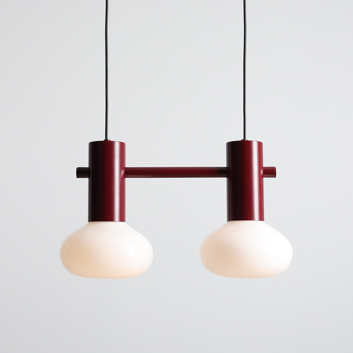 Lampa wisząca Flo Ruby z dwoma kloszami w kolorze mlecznym, zawieszona na czarnym przewodzie. Konstrukcja z metalowych elementów w kolorze czerwonym, z prostym, nowoczesnym designem.